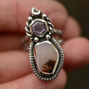 Könnte beinhalten: Ein Silberring mit zwei Edelsteinen. Der obere Stein ist ein sechseckiger lila Amethyst, und der untere Stein ist ein hellrosa und brauner Dendritenachat. Der Ring hat ein detailliertes, strukturiertes Design mit einem Halbmond-Akzent.