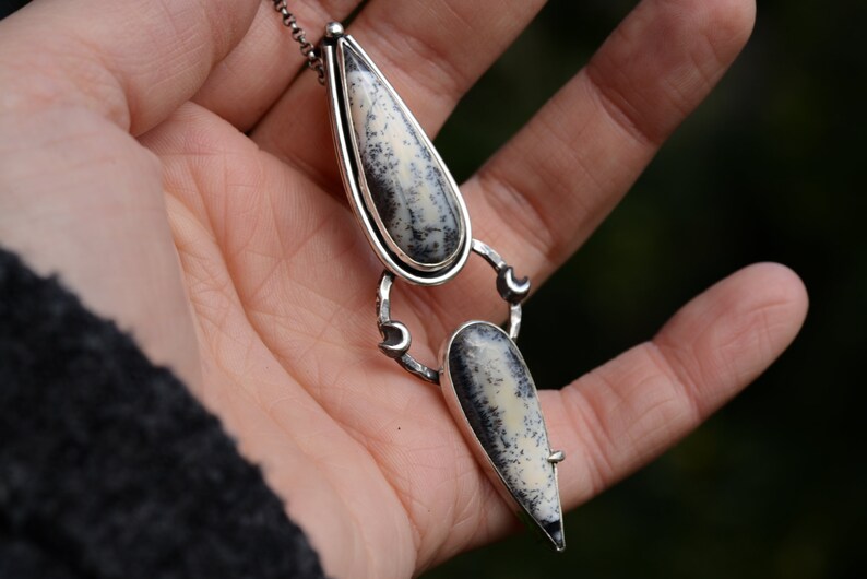 May include: A silver necklace with two teardrop-shaped pendants featuring a white and black dendritic agate stone.
