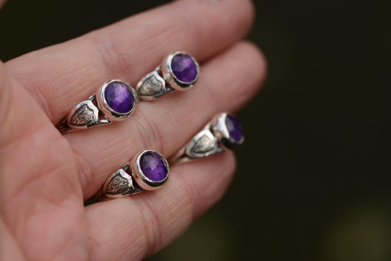 May include: Four silver rings featuring purple amethyst gemstones. The rings have a delicate design with a wing-like detail on the band.