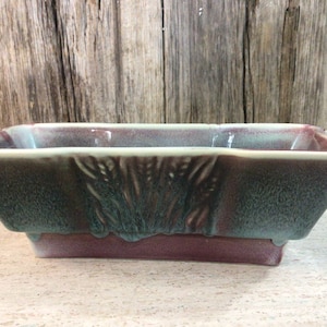 May include: A rectangular ceramic planter with a textured, green and purple glaze. The planter has a slightly raised base.