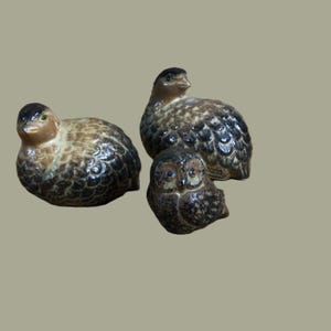 May include: Three ceramic figurines of birds. Two are brown and black with a speckled pattern, and one is a brown and black owl.