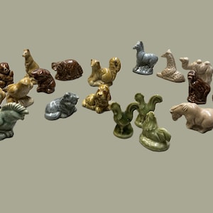 Peut inclure: Une collection de petites figurines d'animaux en céramique de différentes couleurs et poses, incluant un perroquet, un singe, un écureuil, un cheval, un chameau et un coq. Chaque pièce présente une finition émaillée brillante et représente une espèce.