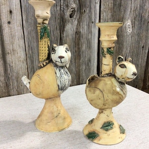 Puede incluir: Un par de candelabros de cerámica con forma de ardillas. Los candelabros están pintados en tonos de marrón, amarillo y verde. Cada ardilla tiene una cara detallada y una cola tupida. Los candelabros son una adición única y caprichosa a cualquier decoración del hogar.
