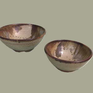 May include: Two ceramic bowls with a brown and white glaze. The bowls are slightly different sizes and have a rustic, handmade look.