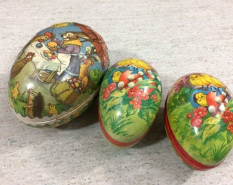 May include: Three vintage Easter egg-shaped boxes with colorful paper coverings. The largest box features a rabbit, chickens, and a hedgehog. The two smaller boxes feature yellow chicks and flowers.