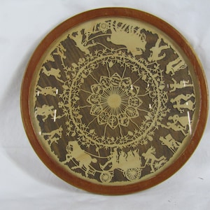 May include: A round wooden frame with a glass insert, showcasing a detailed paper cut design of a horse-drawn carriage and figures in a circular pattern. The design is intricate and features a delicate floral motif.