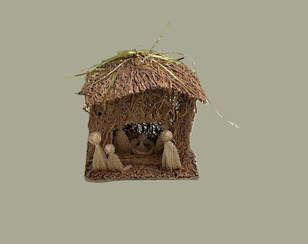 May include: A handcrafted nativity scene, featuring a rustic hut made of woven brown fibers with a thatched roof. Inside, figures of the holy family are visible. The scene is a miniature representation of the Christmas story.