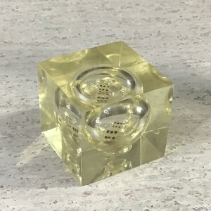 May include: A clear, yellow-tinted cube with two spherical, clear inserts. Each insert contains a set of black dice. The cube is made of a transparent material, allowing the dice to be seen from all angles. A unique decorative item.