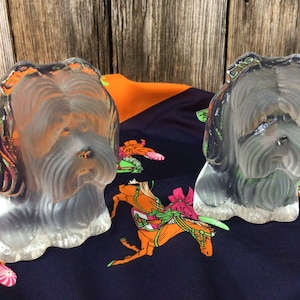 Puede incluir: Dos sujetalibros de vidrio transparente con forma de perro, sobre una tela azul y naranja con diseño de caballo.