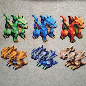 May include: Six pixel art dragons in shades of green, blue, orange, and brown. Each dragon is crafted from small beads, featuring detailed wings and a fierce expression. The dragons are arranged on a grey surface.