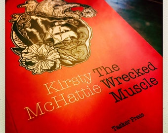 Könnte beinhalten: Ein roter Buchumschlag mit einer Schwarzweißillustration eines Herzens mit einem Schiff darin. Der Titel des Buches lautet "Kirsty McHattie The Wrecked Muscle" und der Verlag ist "Tasker Press".