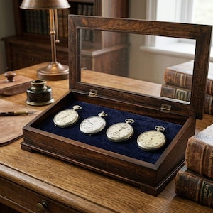 May include: A dark wooden display case with a glass lid, containing four vintage pocket watches. The watches, with white faces and silver casings, are set on a blue velvet base. The case is open, revealing the timepieces.