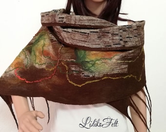 May include: A brown wool scarf with a colorful abstract design and fringe. The scarf is folded and draped around the neck of a person wearing a white shirt.