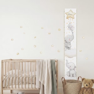 May include: A vertical wall decal growth chart featuring watercolor illustrations of gray elephants, clouds, and a yellow star at the top with the name "Marius" written in script. The design includes small scattered star decals for the wall.