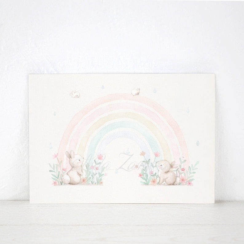 Peut inclure: Une impression d'art rectangulaire pr&eacute;sentant une illustration &agrave; l'aquarelle de deux lapins brun clair assis parmi des fleurs roses et du feuillage vert. Un arc-en-ciel pastel doux surplombe les lapins, avec des gouttes de pluie bleues.