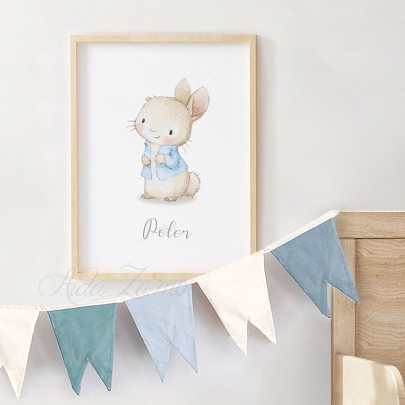 K&ouml;nnte beinhalten: Eine Aquarell-Illustration von Peter Rabbit, der eine blaue Jacke tr&auml;gt. Die Illustration ist in einem hellen Holzrahmen gerahmt und h&auml;ngt an einer wei&szlig;en Wand. Eine blau-wei&szlig;e Girlande h&auml;ngt unter dem Rahmen.