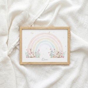 Peut inclure: Un cadre en bois rectangulaire contenant une impression d'un arc-en-ciel pastel, deux petits lapins bruns et des fleurs roses. Le pr&eacute;nom Dana est imprim&eacute; en &eacute;criture cursive au centre en bas. L'illustration pr&eacute;sente des tons aquarelle doux.