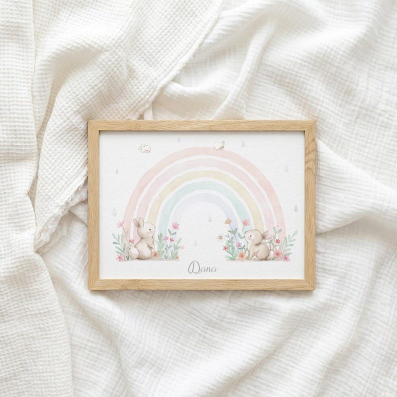 Peut inclure: Un cadre en bois rectangulaire contenant une impression d'un arc-en-ciel pastel, deux petits lapins bruns et des fleurs roses. Le pr&eacute;nom Dana est imprim&eacute; en &eacute;criture cursive au centre en bas. L'illustration pr&eacute;sente des tons aquarelle doux.