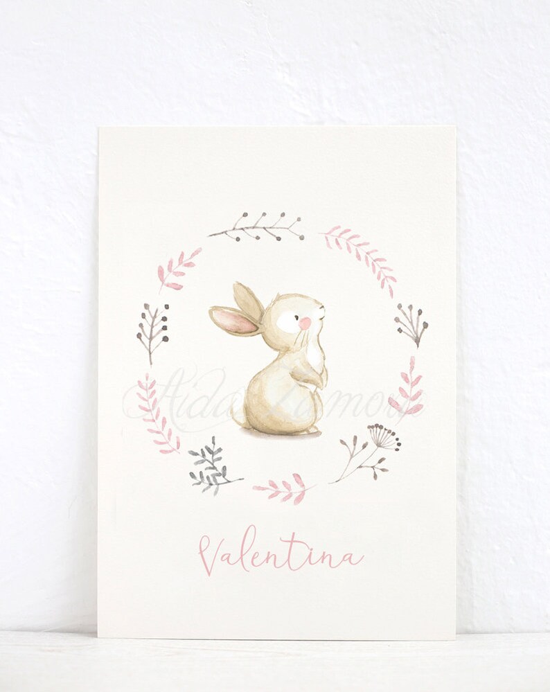 Pu&ograve; includere: Un'illustrazione ad acquerello di un coniglio marrone in piedi in una ghirlanda floreale rosa e grigia. Il nome "Valentina" &egrave; scritto in rosa sotto la ghirlanda.