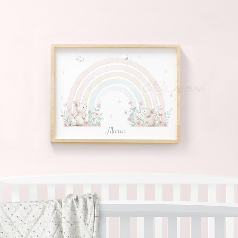 Peut inclure: Une impression murale horizontale encadr&eacute;e pr&eacute;sentant une illustration &agrave; l'aquarelle de deux petits lapins assis dans un champ de fleurs roses sous un arc-en-ciel pastel avec des gouttes de pluie. Le pr&eacute;nom Maria est &eacute;crit en cursif en bas.