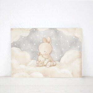 May include: A rectangular wall art print featuring a watercolor illustration of two beige rabbits sitting together on soft, fluffy clouds. The background shows a gray night sky filled with small white stars, creating a gentle and calm scene.