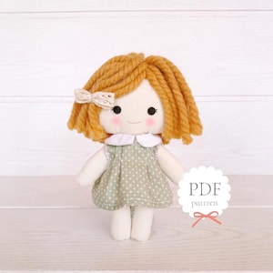 May include: A handmade doll with orange yarn hair, rosy cheeks, and a white bow. The doll wears a green polka-dot dress with a white collar. The image includes the text "PDF pattern".