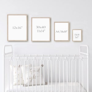 K&ouml;nnte beinhalten: Vier verschiedene Gr&ouml;&szlig;en von Bilderrahmen mit wei&szlig;en Passepartouts und naturfarbenen Holzrahmen. Die Rahmen h&auml;ngen an einer wei&szlig;en Wand &uuml;ber einem wei&szlig;en Kinderbett mit einem wei&szlig;en Kissen mit goldenen Punkten und einem wei&szlig;en Kissen mit dem Text "Gute Nacht".