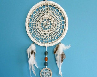Puede incluir: Un atrapasueños de crochet blanco con plumas blancas y cuentas azules y naranjas colgando de él. El atrapasueños está colgado en una pared azul.