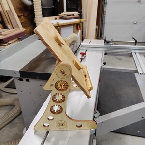 May include: A wooden stand with a tilting top, designed for holding a laptop or tablet. The stand has a unique design with multiple circular cutouts and a gear-like pattern.