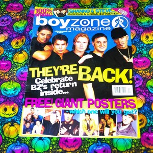 May include: A Boyzone magazine with the headline "THEY'RE BACK!" and images of the band. The magazine is on a patterned fabric with colorful jack-o'-lanterns.