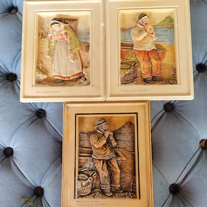 May include: Three framed relief sculptures depicting scenes of Cornish fishermen. One shows a woman unloading a boat, another a fisherman waiting for the tide, and the third a fisherman with the text "Cornish fisherman waiting for the tide."