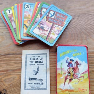 Op de afbeelding: Een vintage kaartspel, "Riders of the Range", met kleurrijke kaarten en dooskunst. De kaarten bevatten illustraties van een ranch en een cowboy te paard. Inclusief een regelvel en een kaartspel met nummers.