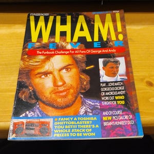 May include: A retro magazine cover for "WHAM! FEVER" with a portrait of George Michael. The cover has yellow and blue text, including "The Funbook Challenge" and other promotional text. A small image of Andrew Ridgeley is also present.