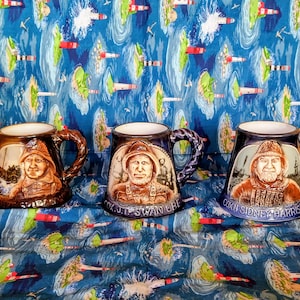 May include: Three ceramic mugs with detailed relief portraits of men in maritime attire. The mugs have textured handles and are brown, blue, and white. Each mug features a different portrait and name, with the text "COXN J.T. SWAN OBE" and "COXN SIDNEY HARRIS R.N."