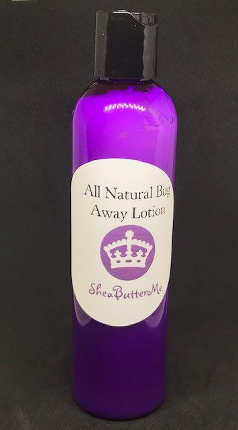 Peut inclure: Une bouteille violette de lotion anti-moustiques enti&egrave;rement naturelle avec une &eacute;tiquette blanche repr&eacute;sentant une couronne et le texte "Shea Butter Me".