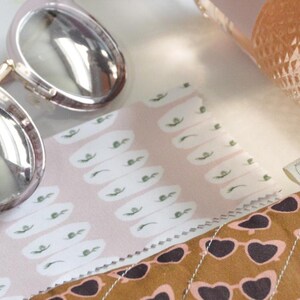 May include: A collection of accessories including sunglasses, a wine bottle, and a book. The sunglasses have a gold frame and silver lenses. A brown glasses case with a heart-shaped sunglasses pattern is also present.