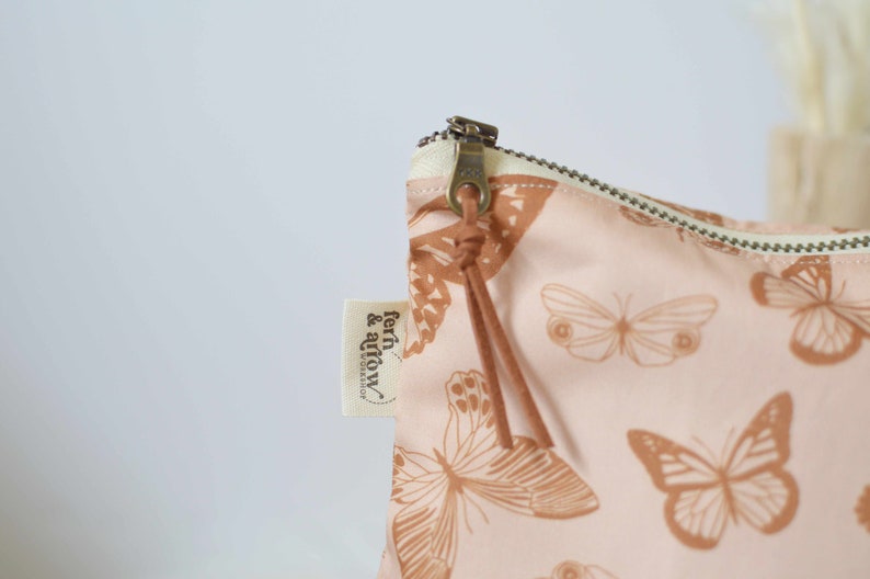 Water resistant bag with metal YKK zipper and suede tassel. The bag is pink with a rusty colored monarch butterfly print. The lining on the bag is PUL lining and is water resistant.