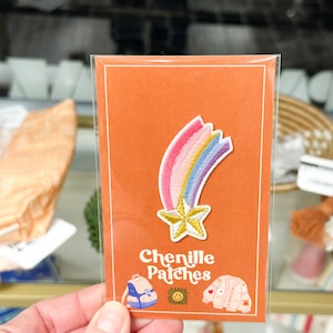 May include: A rainbow chenille iron-on patch with a gold star. The patch is on a card with the text "Chenille Patches" and images of other patches.