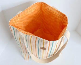 May include: A striped tote bag with a cream-colored handle and a brown tag. The bag features vertical stripes in orange, blue, and yellow. The interior lining is orange with a grid pattern.