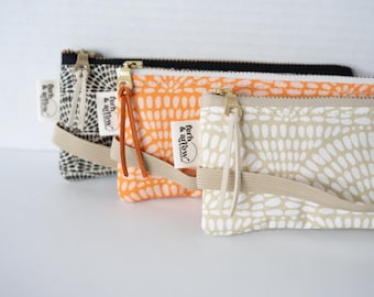 May include: Three rectangular zippered pouches featuring a repeating white dot pattern on black, orange, and beige fabric. Each pouch includes a metal zipper with a leather pull tab, a beige elastic band, and a white fabric tag labeled fern & arrow.