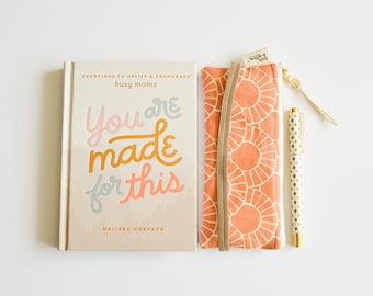 May include: A peach-colored zippered pouch with a white and peach geometric pattern. A white pen with gold polka dots and a devotional book titled "You are made for this" by Melissa Horvath.