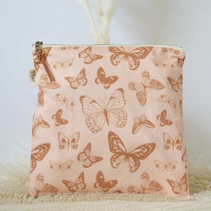 Water resistant bag with metal YKK zipper and suede tassel. The bag is pink with a rusty colored monarch butterfly print. The lining on the bag is PUL lining and is water resistant.