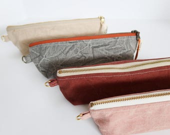 May include: Four zippered pouches in different colors and fabrics. The top pouch is beige, the second is gray with an orange zipper, the third is red, and the bottom pouch is pink.