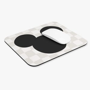 Può includere: Un mouse per computer bianco appoggiato su un tappetino per mouse a scacchi bianco e nero con una silhouette nera della testa di Topolino.
