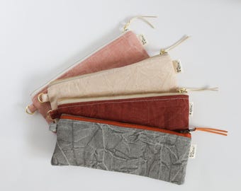 May include: Four rectangular zippered pouches arranged in a stack. The pouches are colored dusty pink, beige, dark red, and textured gray. Each features a metal zipper with a pull tab and a small white fabric tag labeled Fern & Willow.