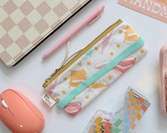 May include: An assortment of stationery and office supplies, including a pink mouse, pen, and a pencil case with a sneaker pattern. A checkerboard pattern is visible on a tablet case and tape dispenser. The pencil case has the text "Fork & Glow".