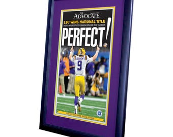 May include: Framed print of a magazine cover with the headline "LSU WINS NATIONAL TITLE." The cover features a football player in a yellow and purple uniform with the word "PERFECT!" in large letters. The frame is dark blue with a purple mat.