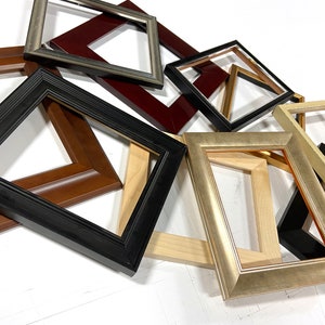 May include: An assortment of picture frames in various colors and styles. Frames include black, brown, gold, and silver finishes. The frames are rectangular and of different sizes, with visible wood grain and ornate detailing.