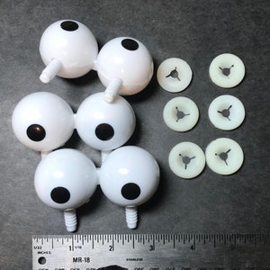 May include: Three pairs of white plastic googly eyes with black pupils. Each eye has a small plastic tube protruding from the back. There are also six white plastic washers with three holes each.