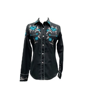 Puede incluir: Camisa negra con botones y bordado floral turquesa. La camisa de manga larga presenta costuras blancas a lo largo de las costuras, el cuello y los puños. El diseño floral incluye flores turquesas y hojas gris plateado.